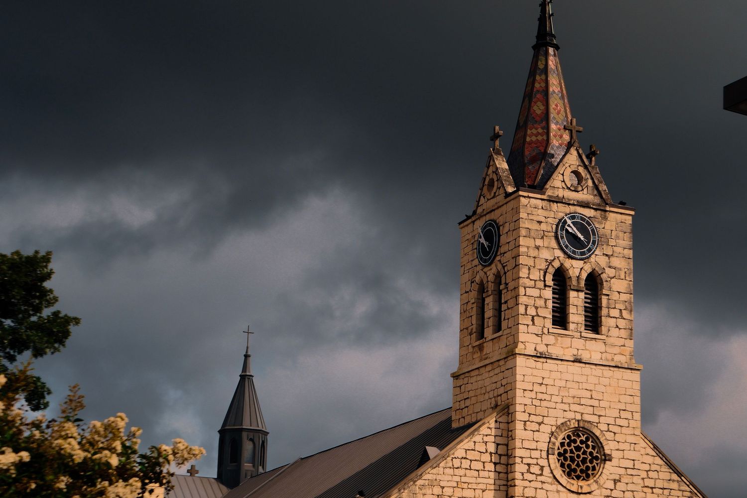 Historic stone church tower with clock under dramatic dark stormy sky.