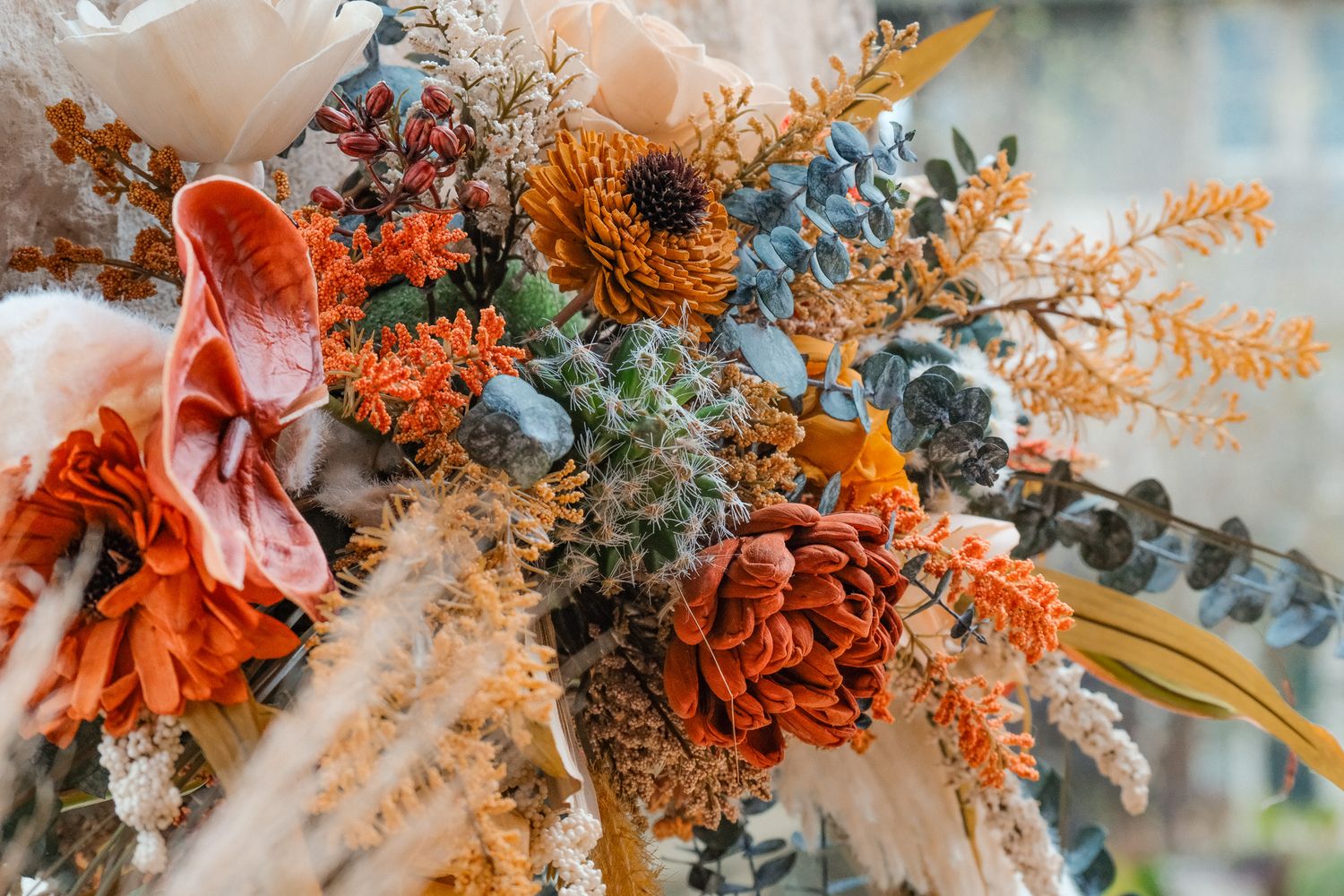 A vibrant wedding bouquet featuring orange, rust, and blue dried and fresh flowers with eucalyptus accents.