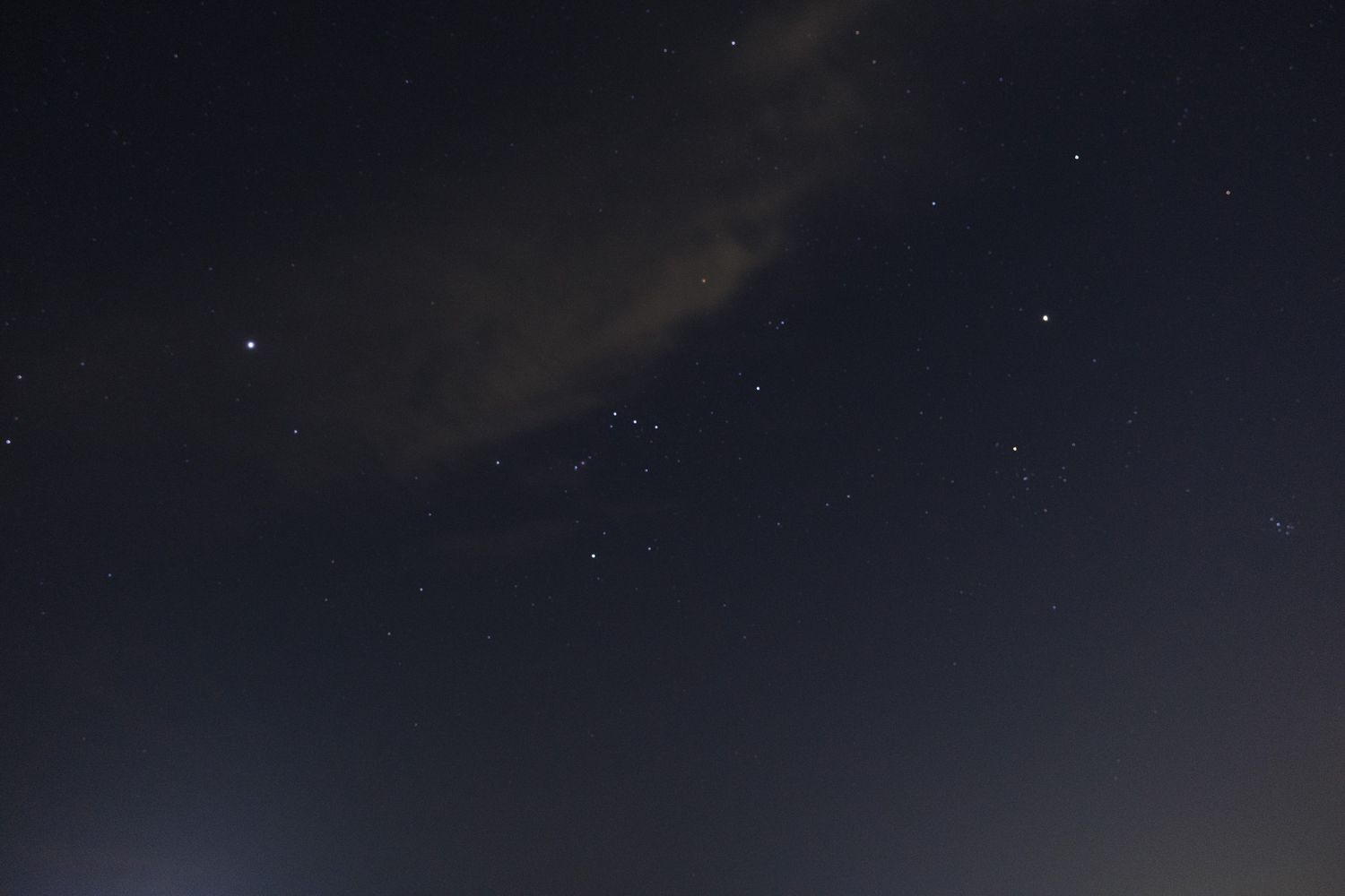 Dark night sky filled with scattered stars and wispy clouds in long exposure photo.
