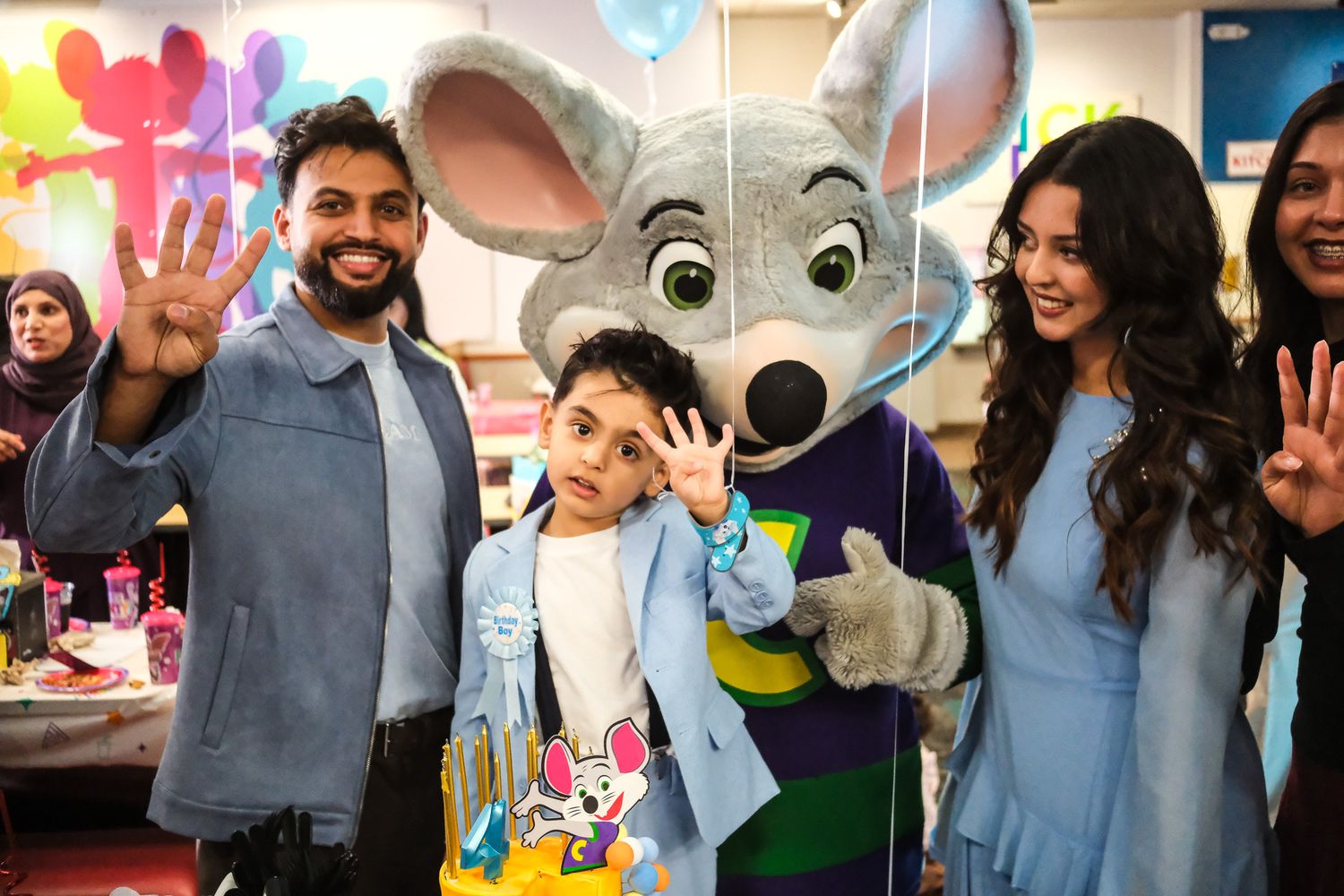 Family posing with Chuck E. Cheese mascot at a colorful birthday party celebration.