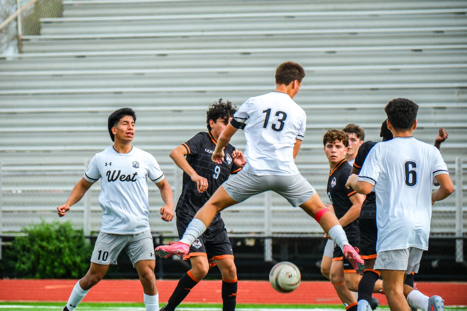 High school soccer players competing for the ball during an intense match on a red track field.