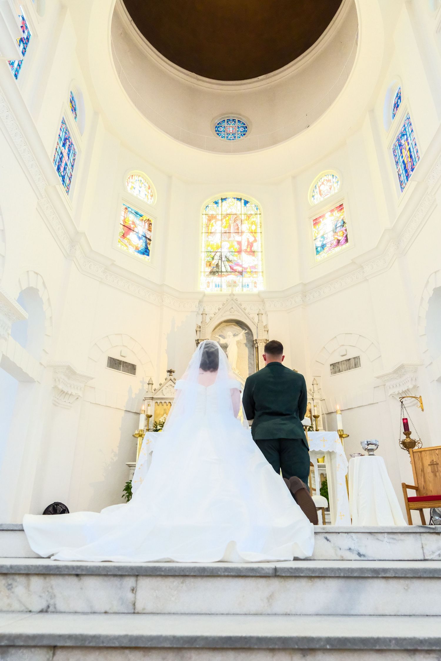 Bride and groom standing at church altar with stained glass windows during wedding ceremony.