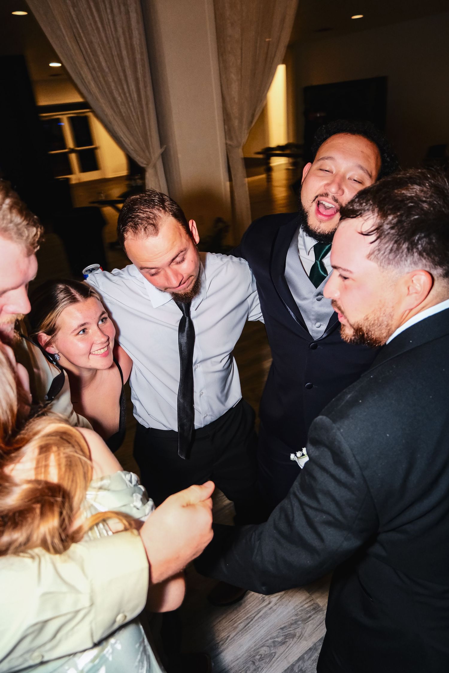 Group of friends laughing and celebrating together at a wedding reception in a dimly lit venue.
