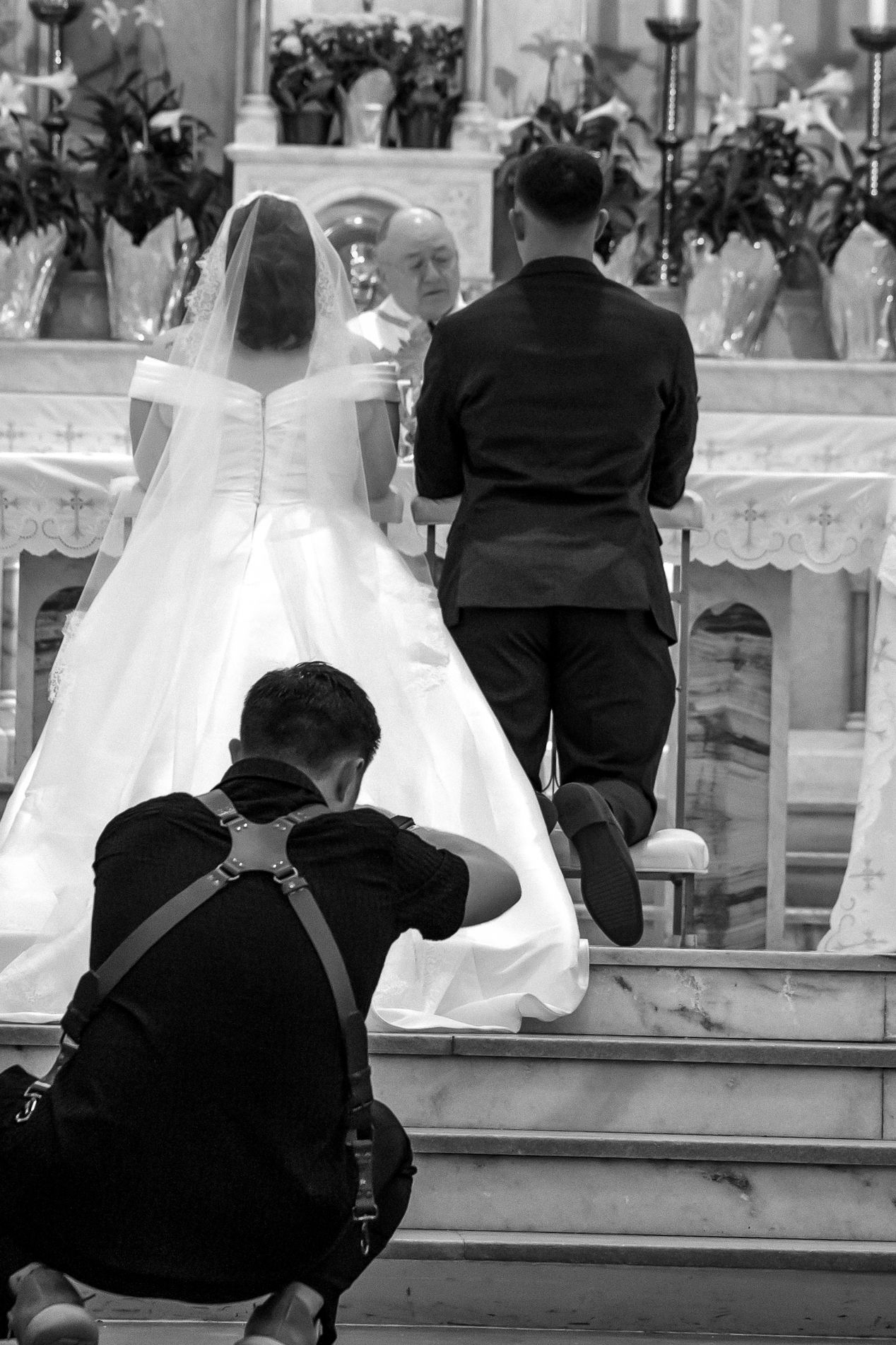 Wedding photographer capturing bride and groom at church altar during ceremony in black and white photograph.