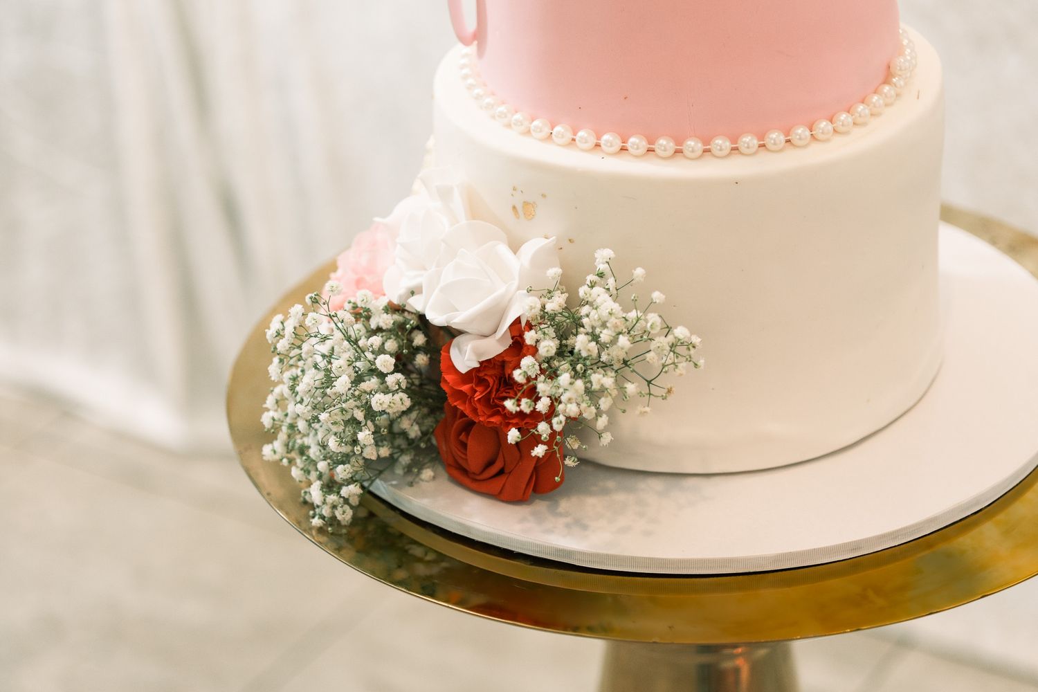White and pink two-tier wedding cake decorated with pearl trim and red, pink, and white floral accents.
