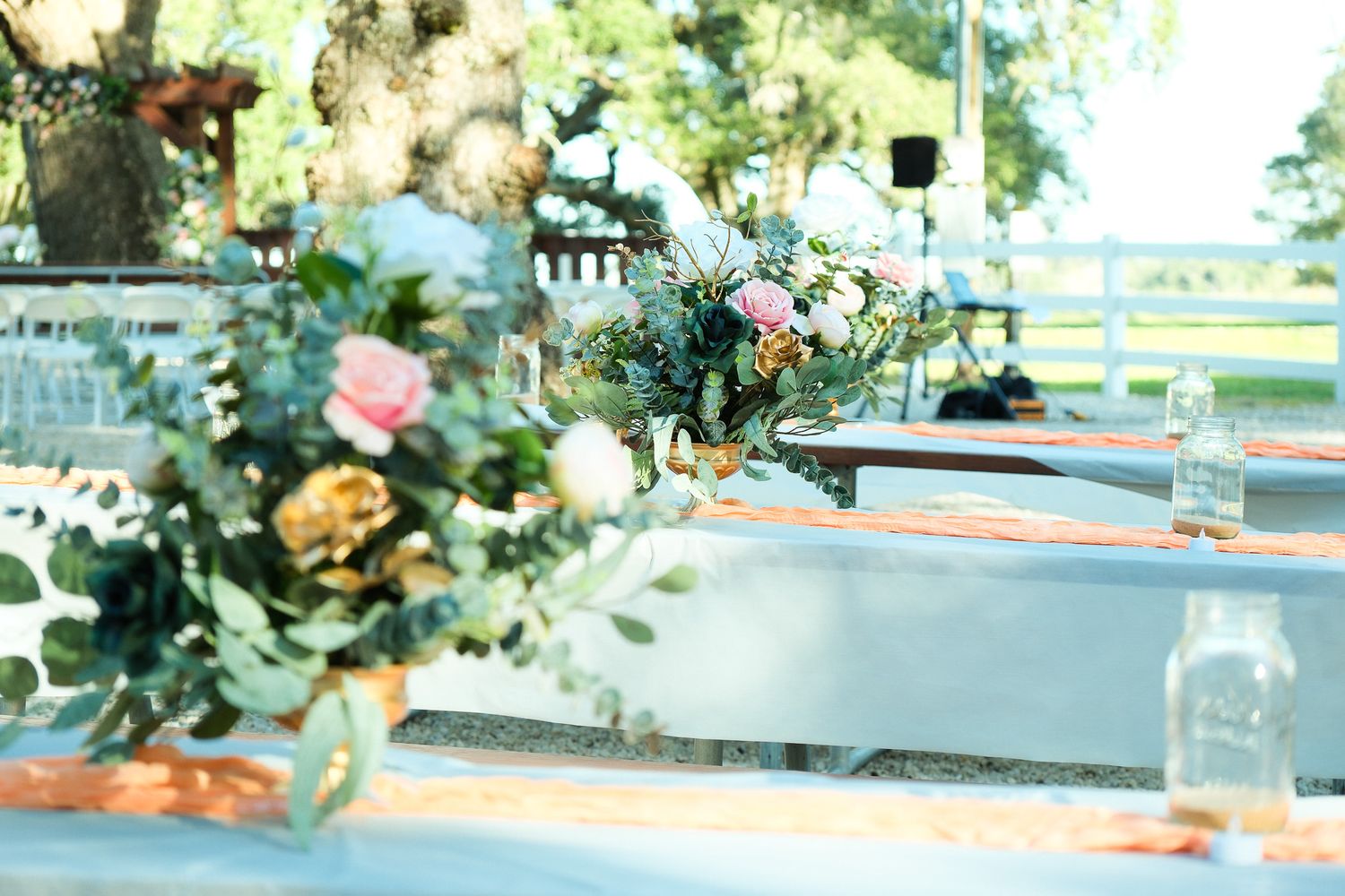 Elegant outdoor wedding reception table decorated with lush floral arrangements featuring pink roses and greenery.
