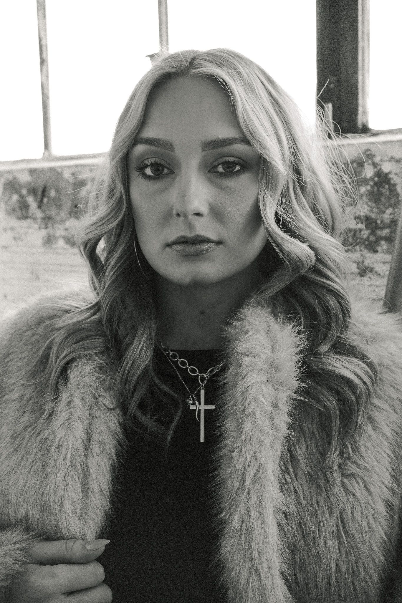 Black and white portrait of a blonde woman in a fur coat wearing a cross necklace.