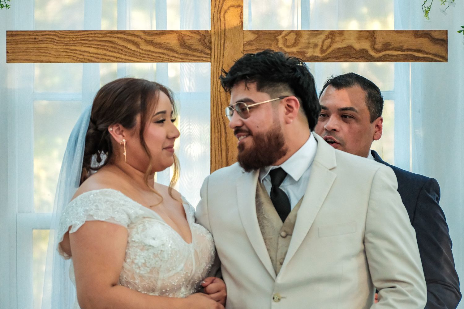 Bride and bearded groom share a joyful moment at the altar with wooden cross backdrop at wedding.