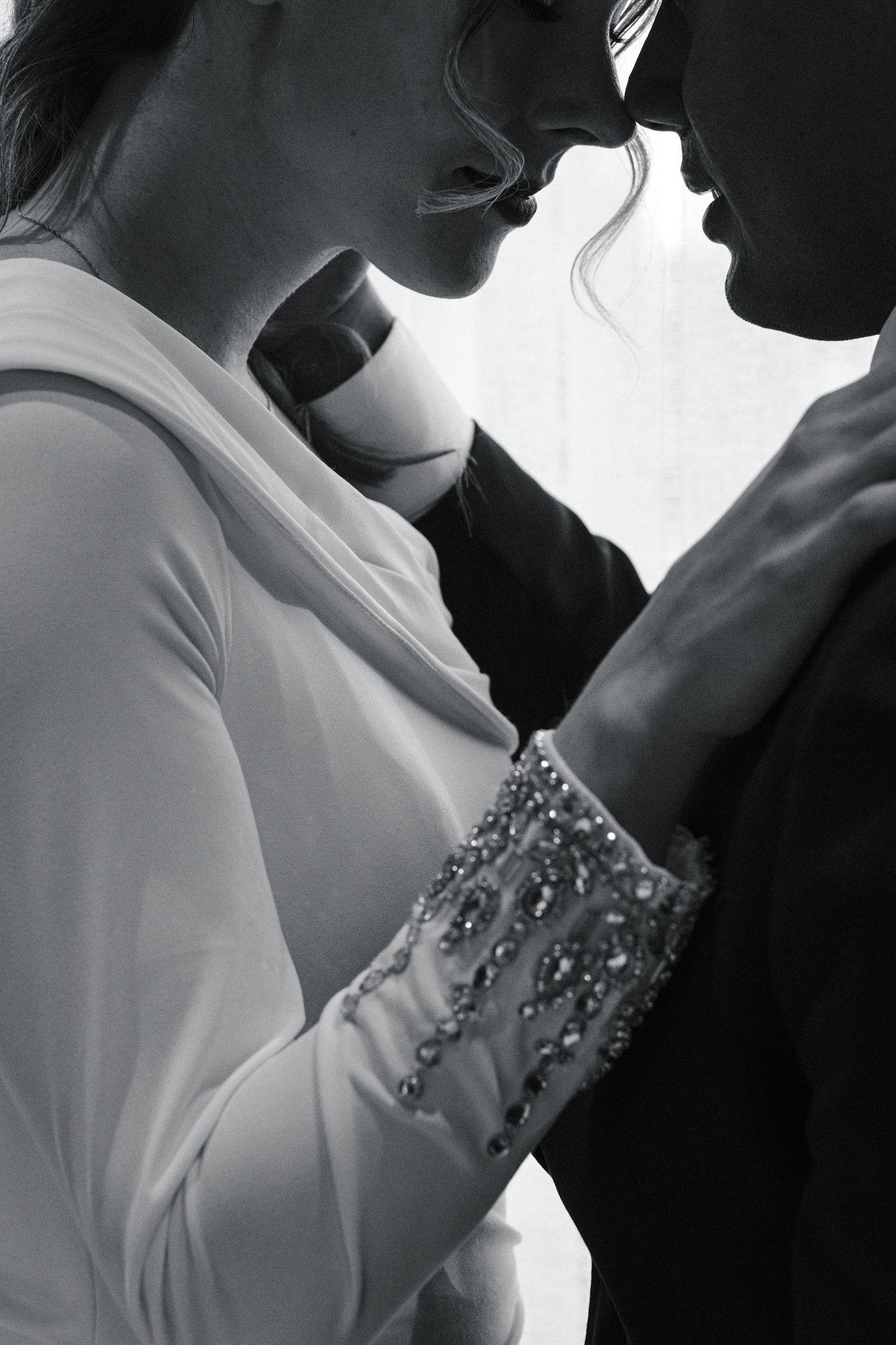 Black and white photo of a couple in formal wear sharing an intimate moment, bride wearing beaded gown detail.