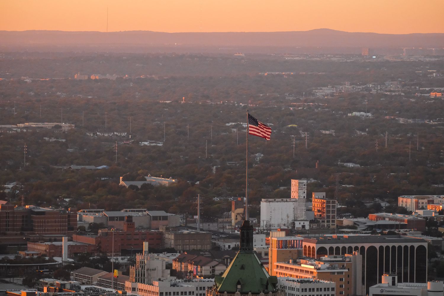 Aerial view of American flag flying over a city skyline at golden sunset hour.