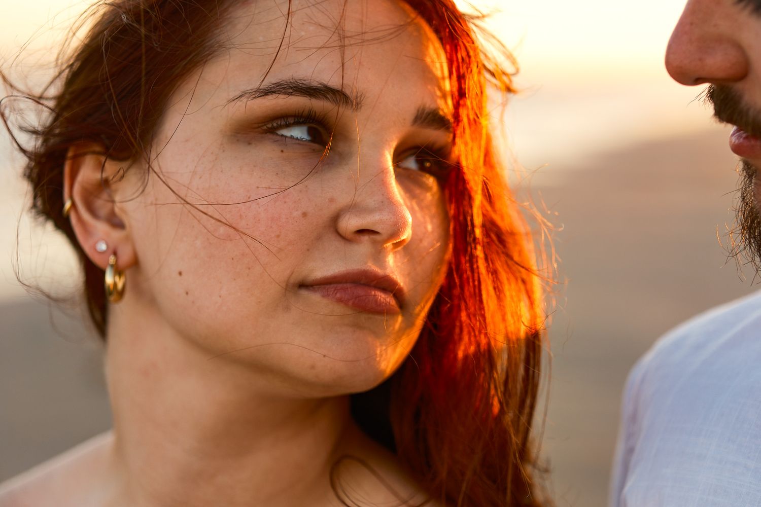 Young woman with freckles and red hair bathed in golden sunset light gazes thoughtfully.