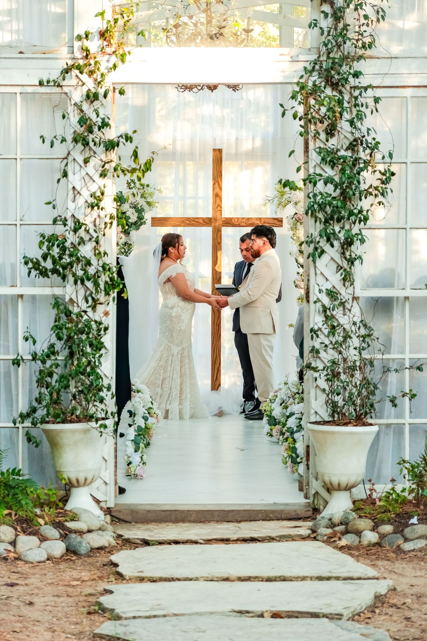Bride and groom exchanging vows at romantic greenhouse wedding altar with wooden cross.