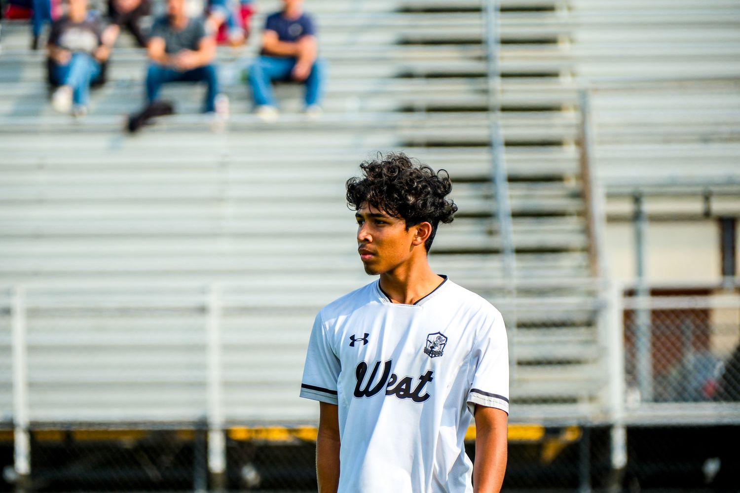 Young soccer player in West team white uniform standing focused on the field during a game.