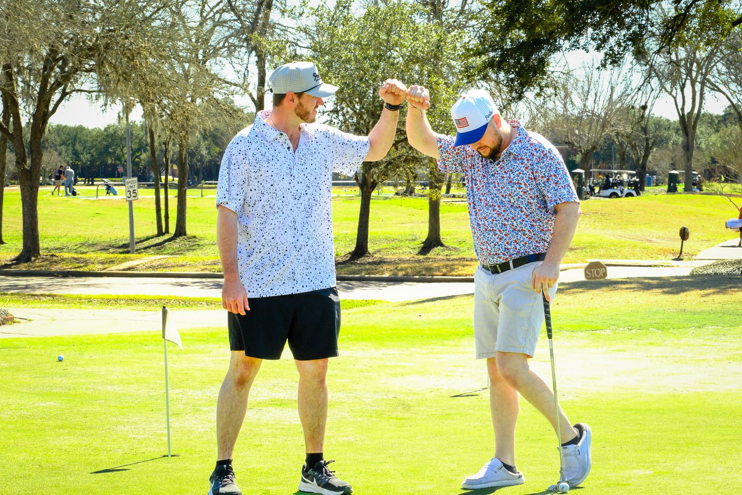 Two men in matching golf shirts fist bumping on a sunny golf course.