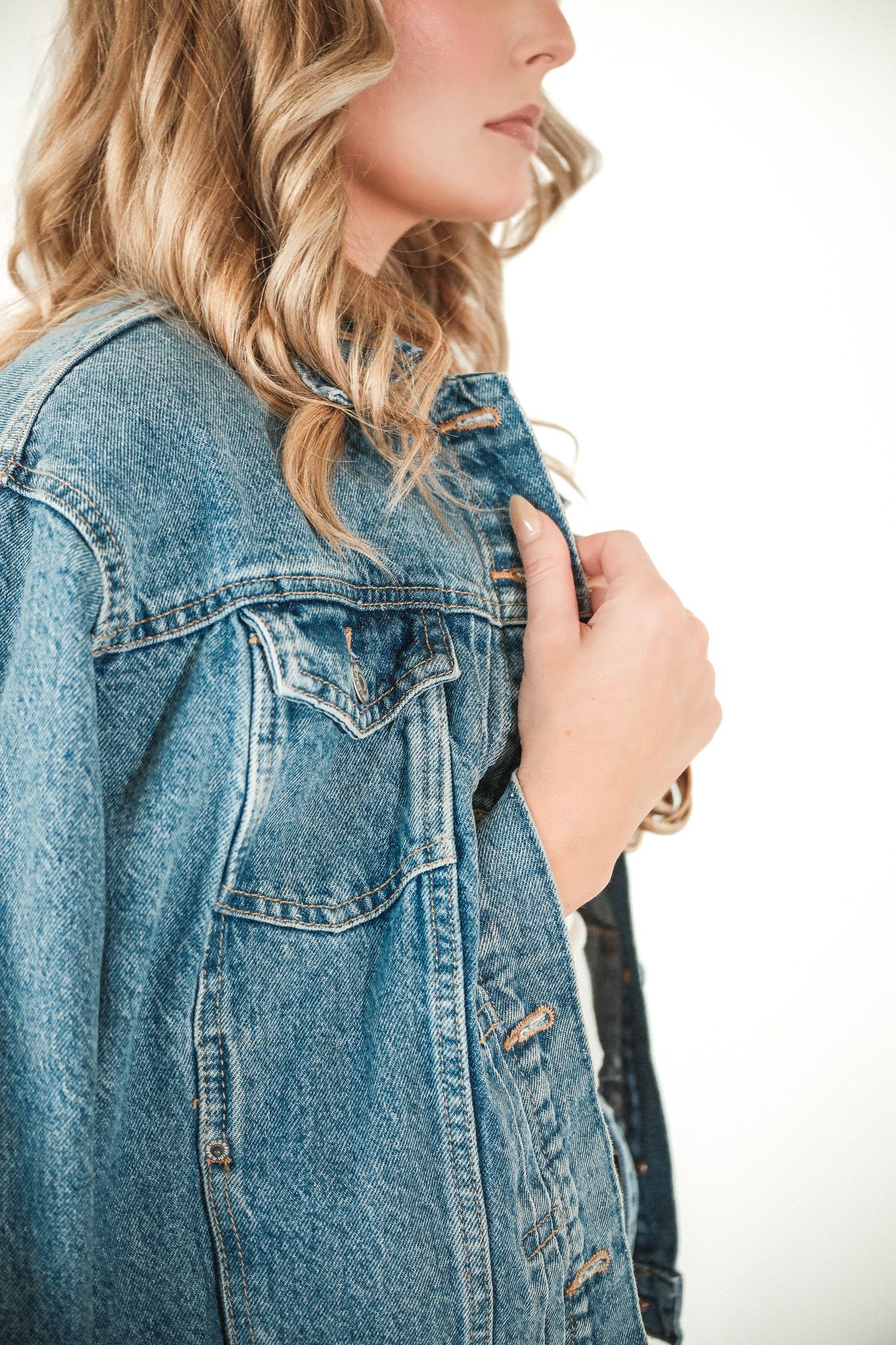 Close-up of a woman in a blue denim jacket with wavy blonde hair against a white background.