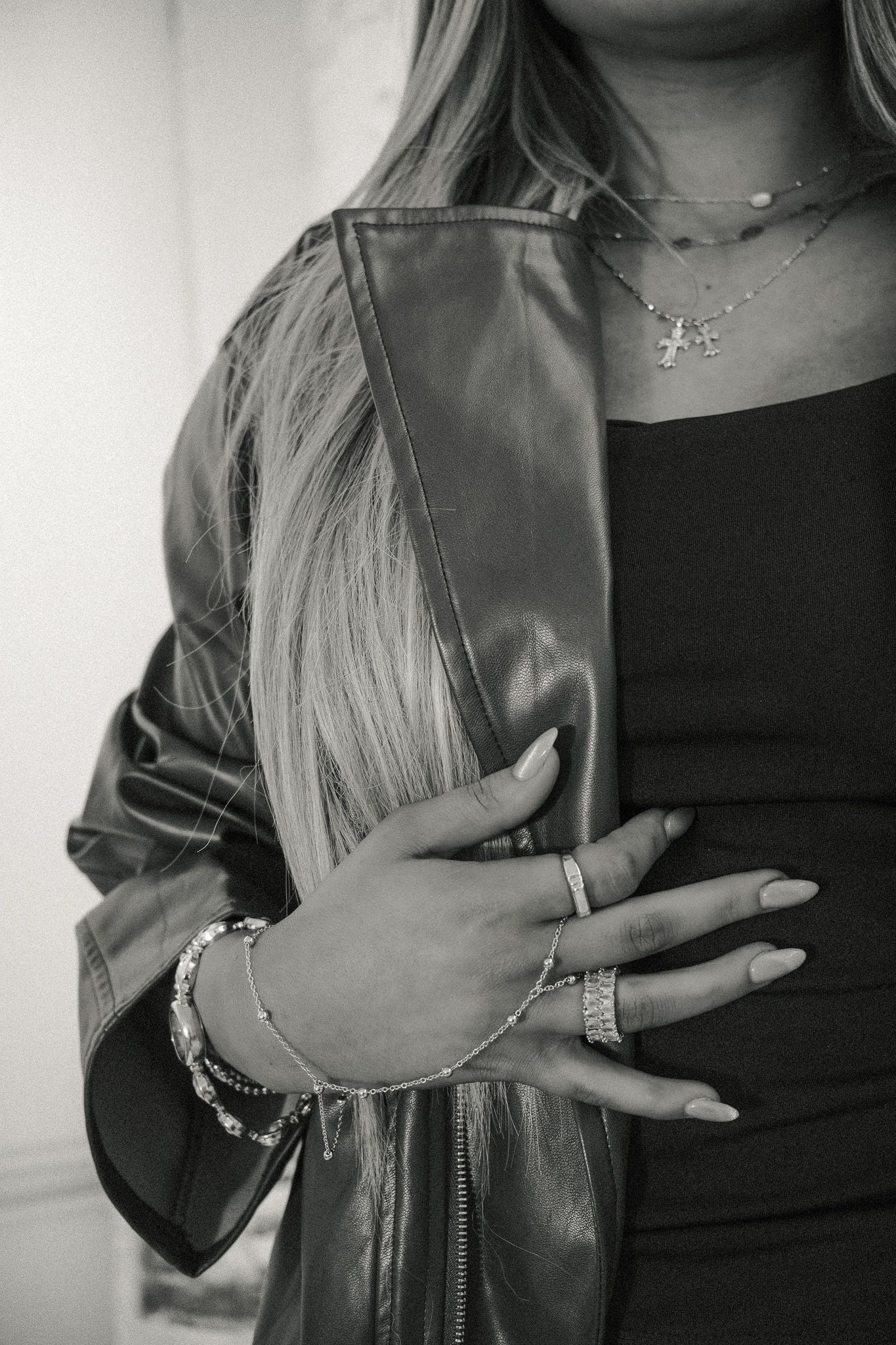 Black and white close-up of woman wearing leather jacket, layered necklaces, and bracelets.