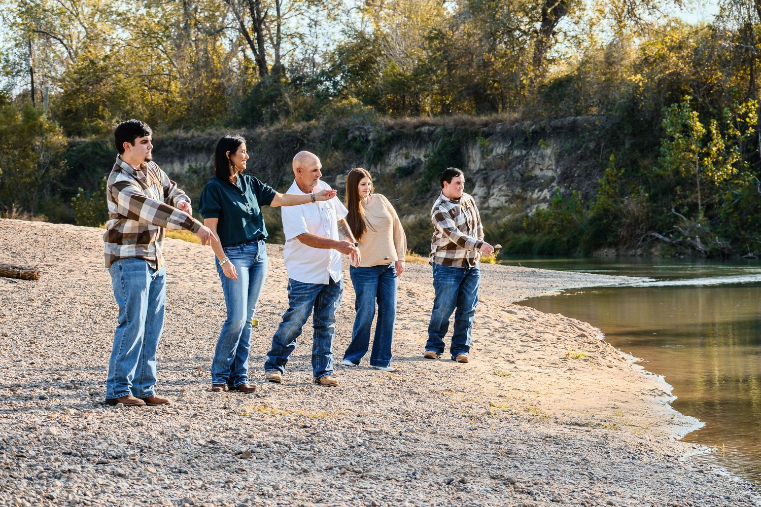 Group of five people fishing together on a rocky riverbank surrounded by autumn trees.