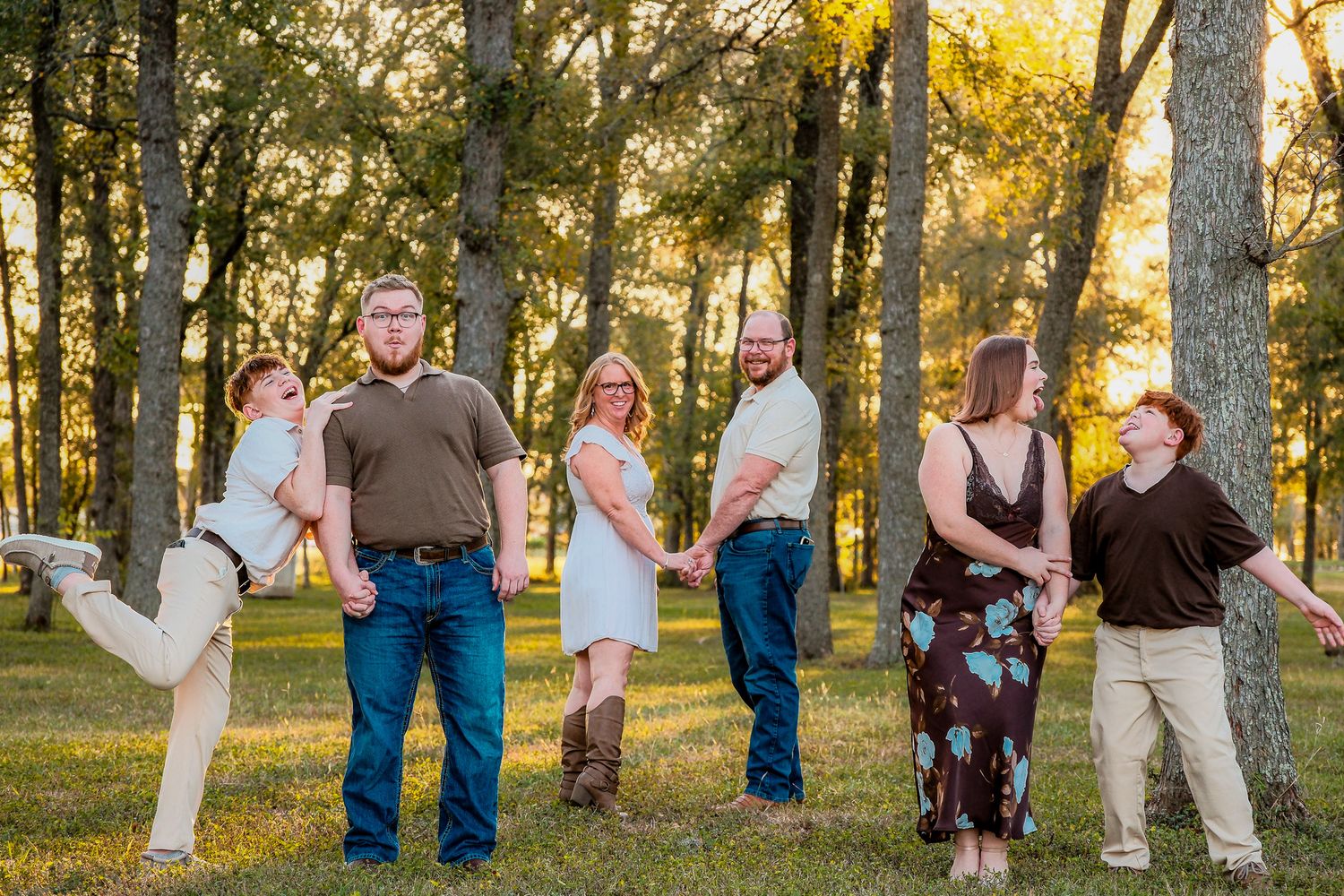 Fun family portrait with six people holding hands in a sunny green wooded park.