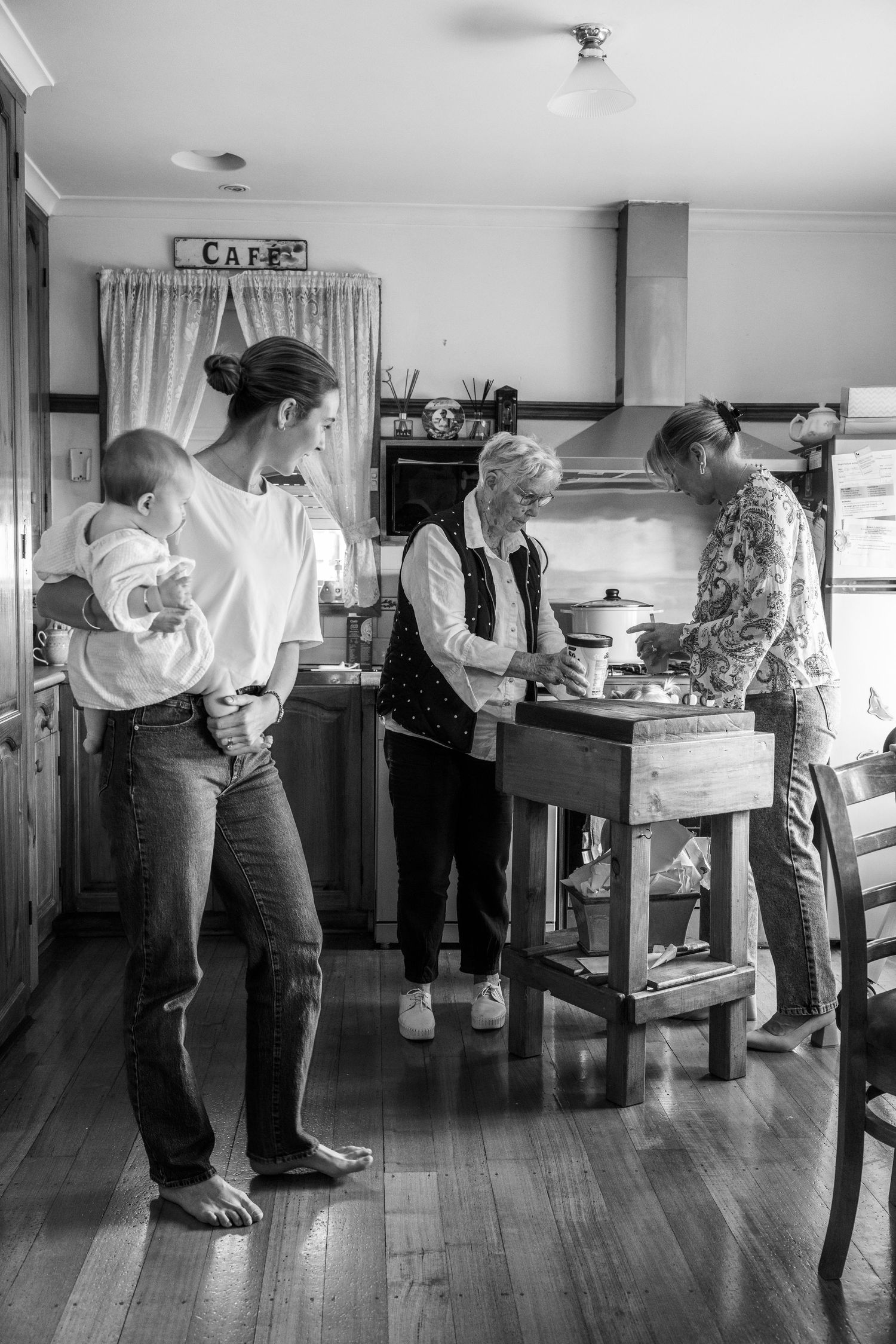 Black and white photo of three generations of women cooking together in a farmhouse kitchen.