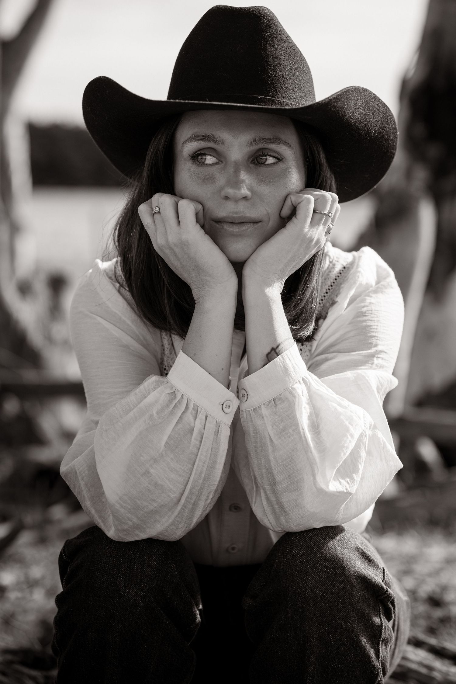 Black and white portrait of a woman in a cowboy hat resting her chin on her hands.