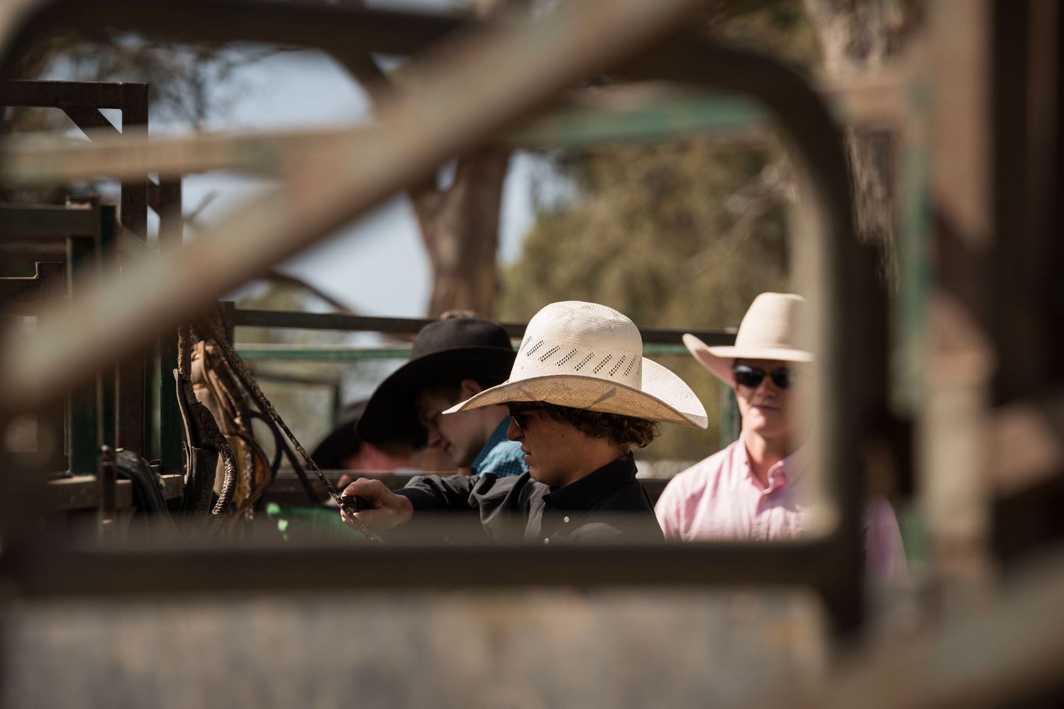People wearing wide-brim hats gather around equipment at an outdoor rodeo event.