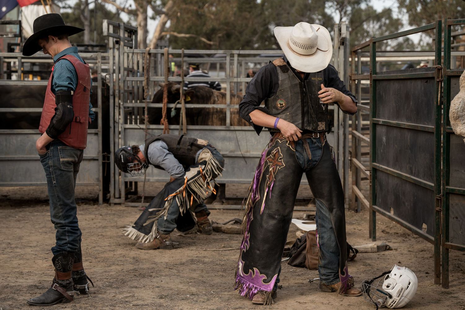 Cowboys in chaps prepare their gear backstage at a dusty outdoor rodeo event.