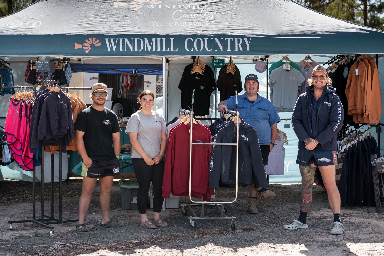 Four staff members posing outside Windmill Country clothing tent display at outdoor country event.