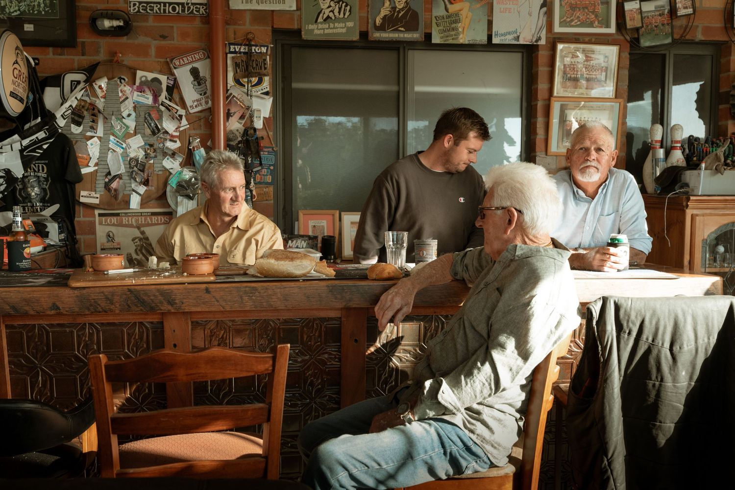 Three men having a conversation at a rustic wooden bar in a cozy, memorabilia-filled tavern.