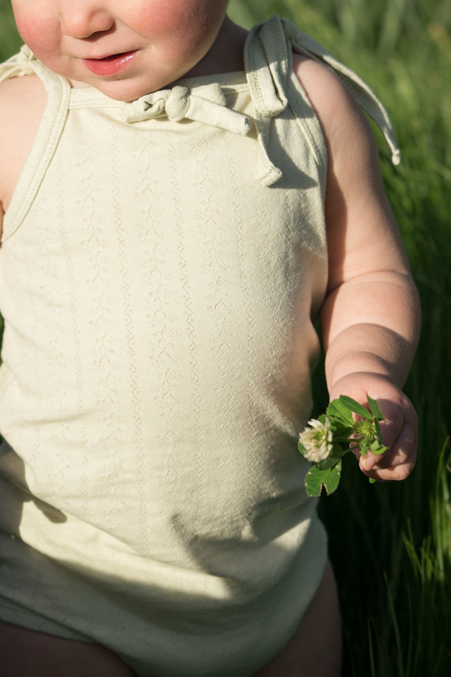 Close-up of toddler in cream knit top holding a small white clover flower outdoors.