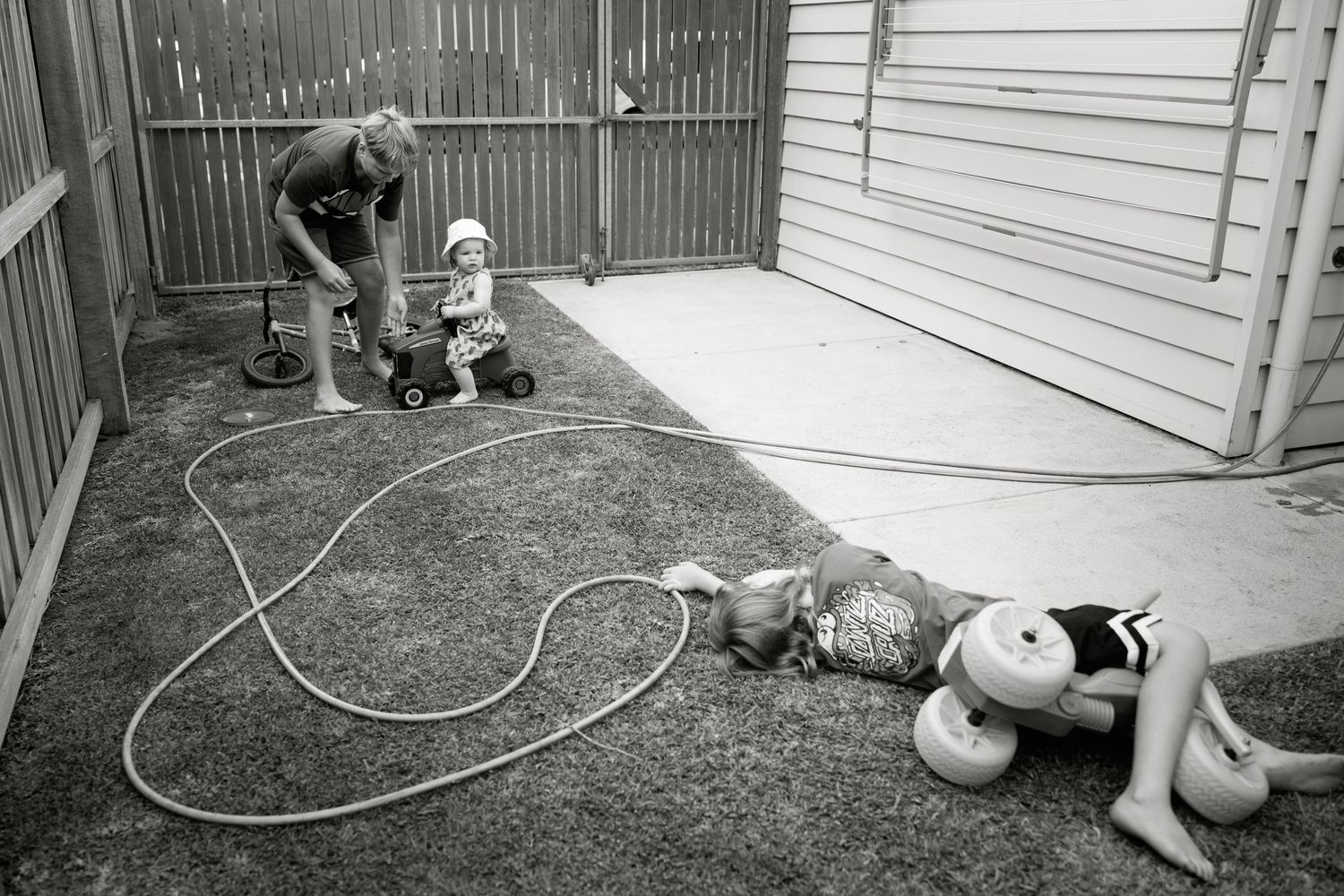 Children playing with a garden hose in a backyard in black and white photography.