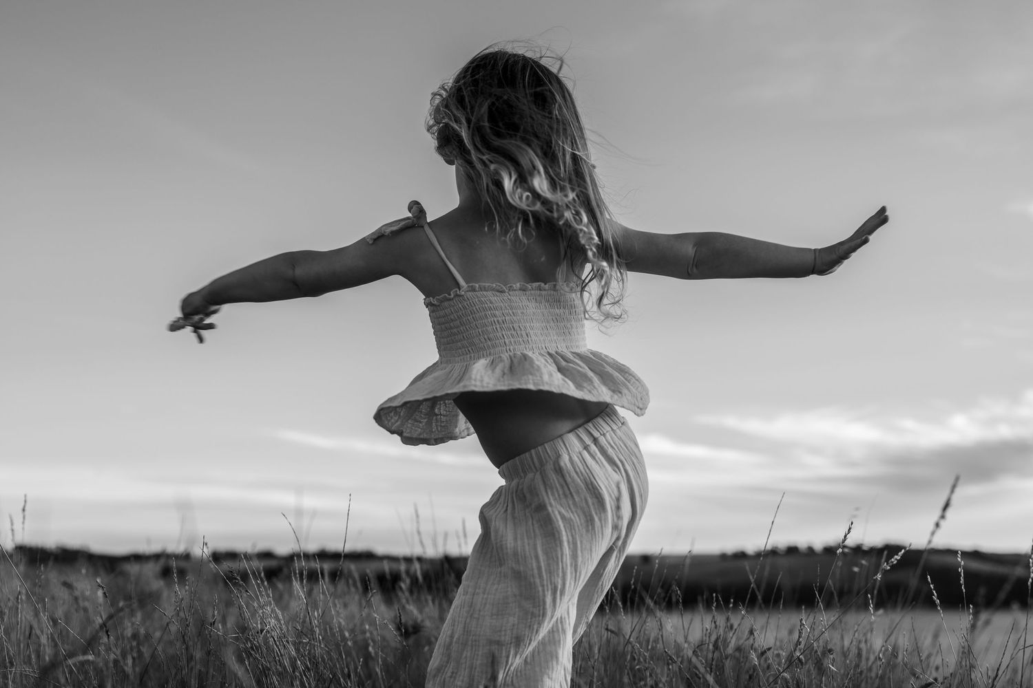 Black and white image of a young girl dancing freely in an open field at dusk.