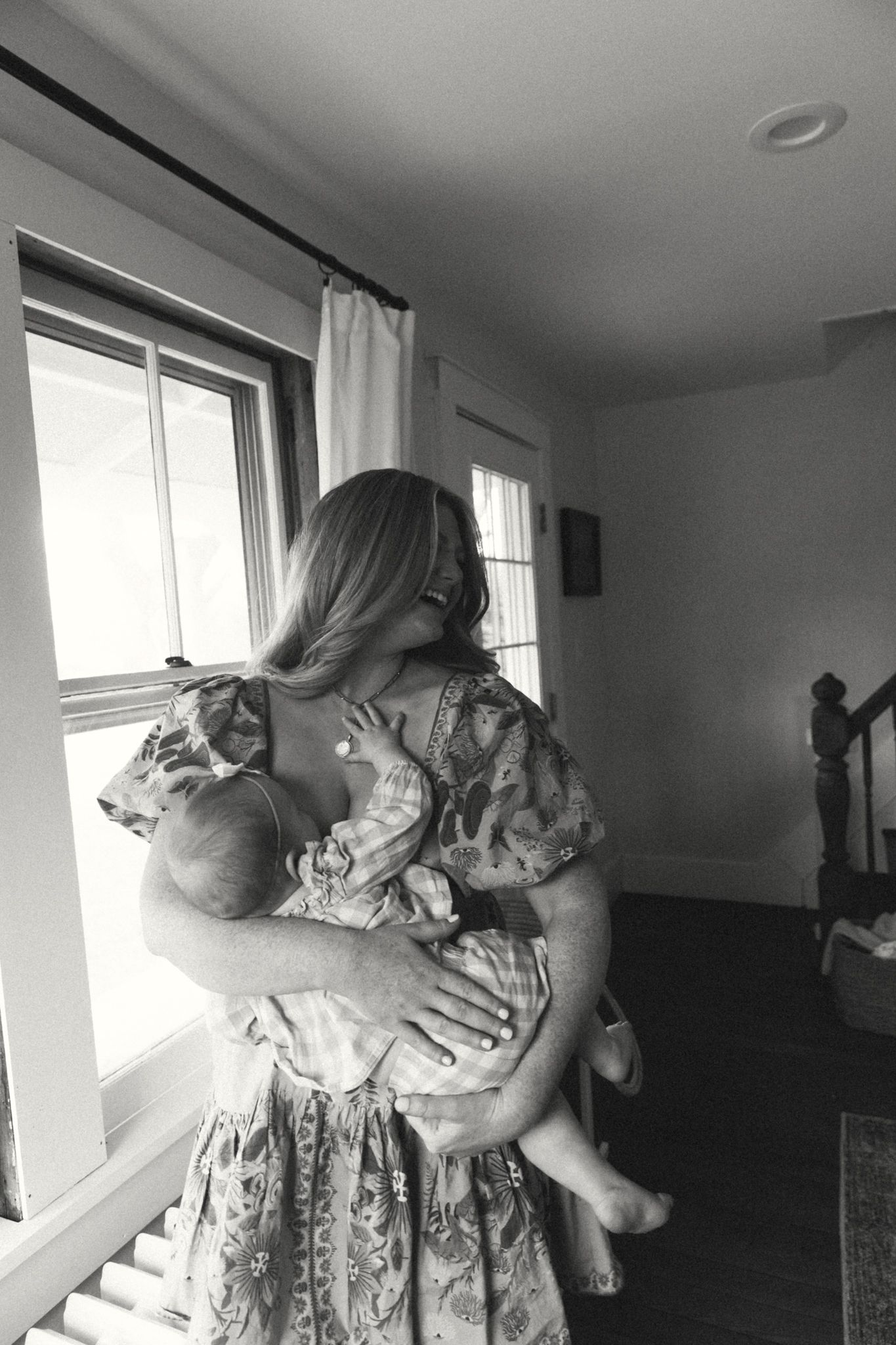 A gray cat is being held and cuddled in a sunlit room with white walls.