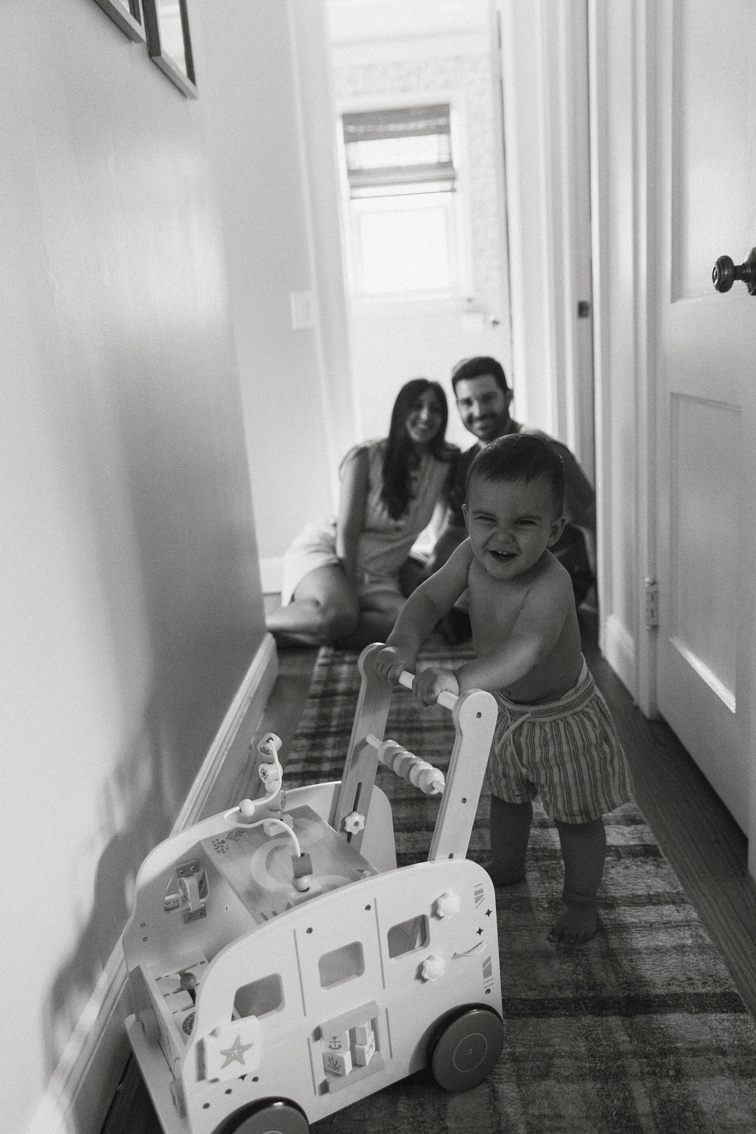 Children playing with a toy vehicle in a bright indoor hallway.