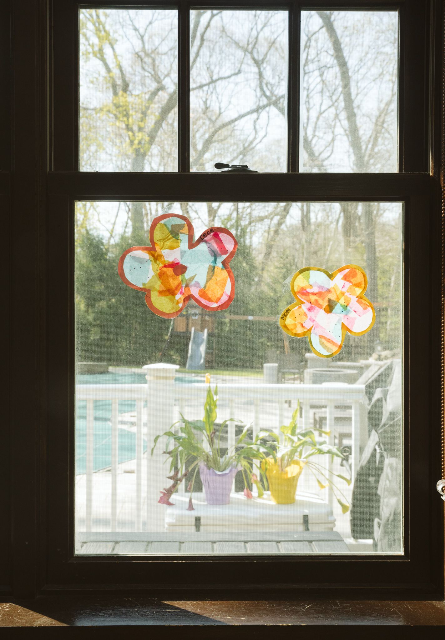 Colorful paper butterflies and flowers decorate a window overlooking a deck with potted plants.