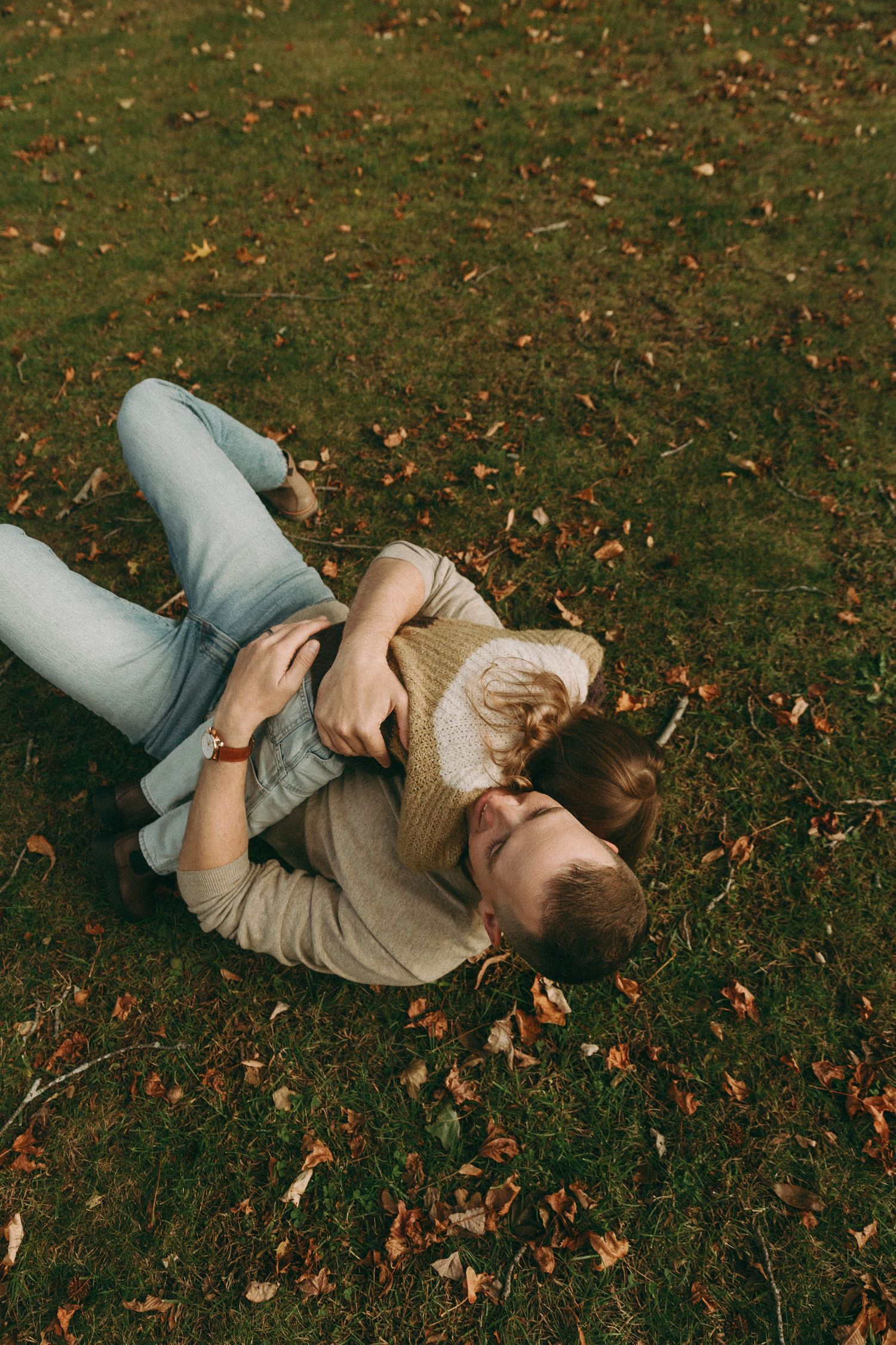 Couple lying on autumn grass, embracing romantically among fallen leaves in a park during fall season.