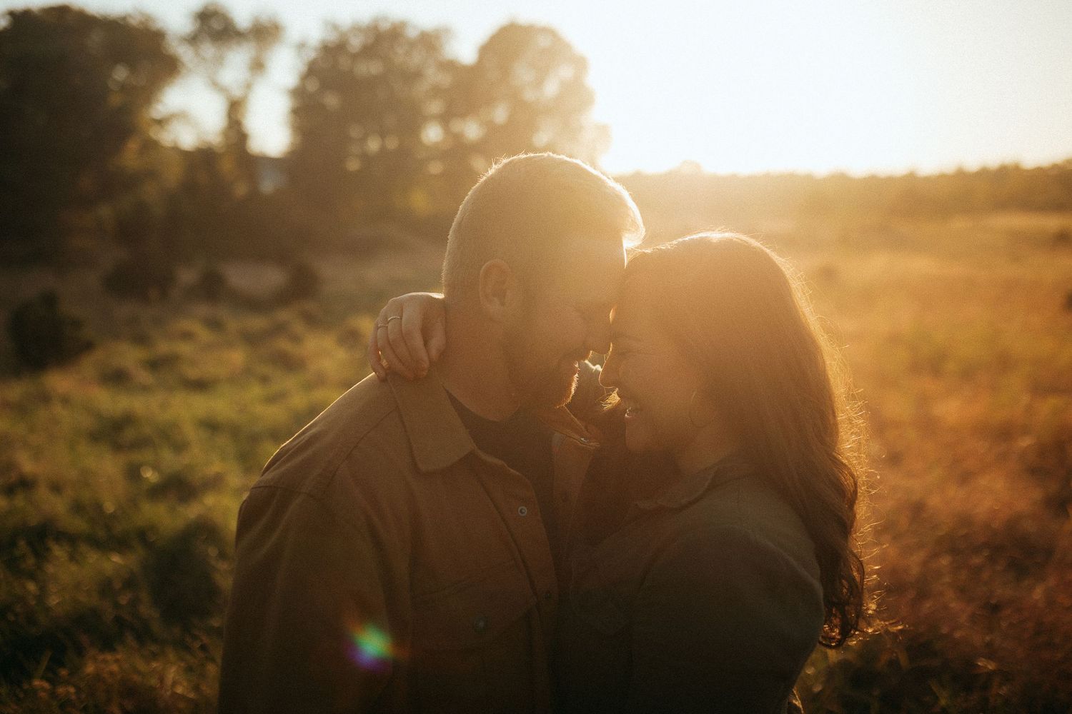 Romantic couple sharing an intimate moment at golden hour in a sunlit field with warm bokeh background.