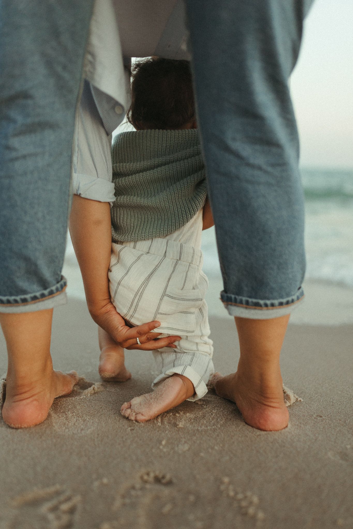 Bare feet of different sizes standing together on sandy beach.