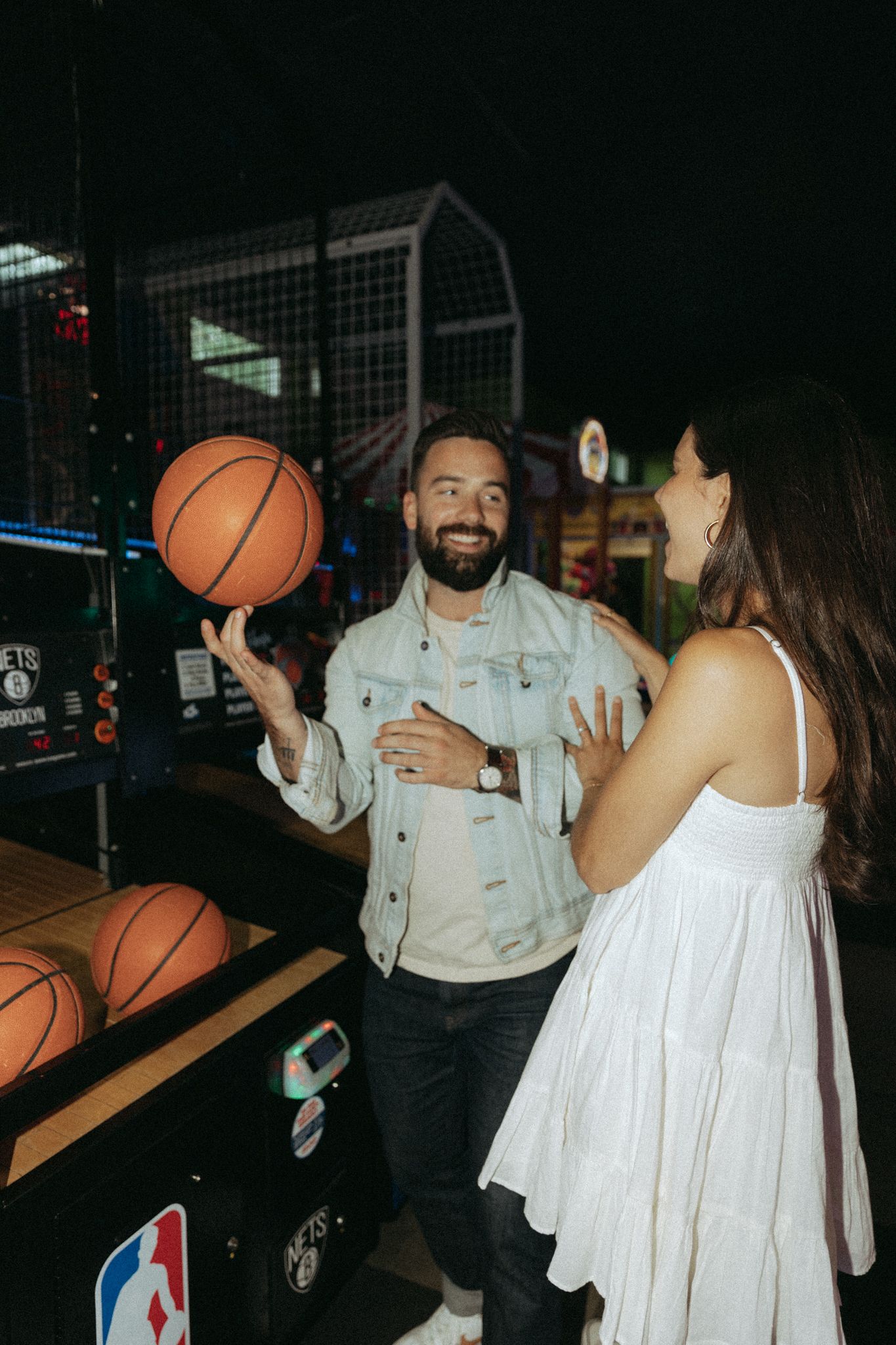 Couple playing basketball arcade game in a dimly lit entertainment venue.