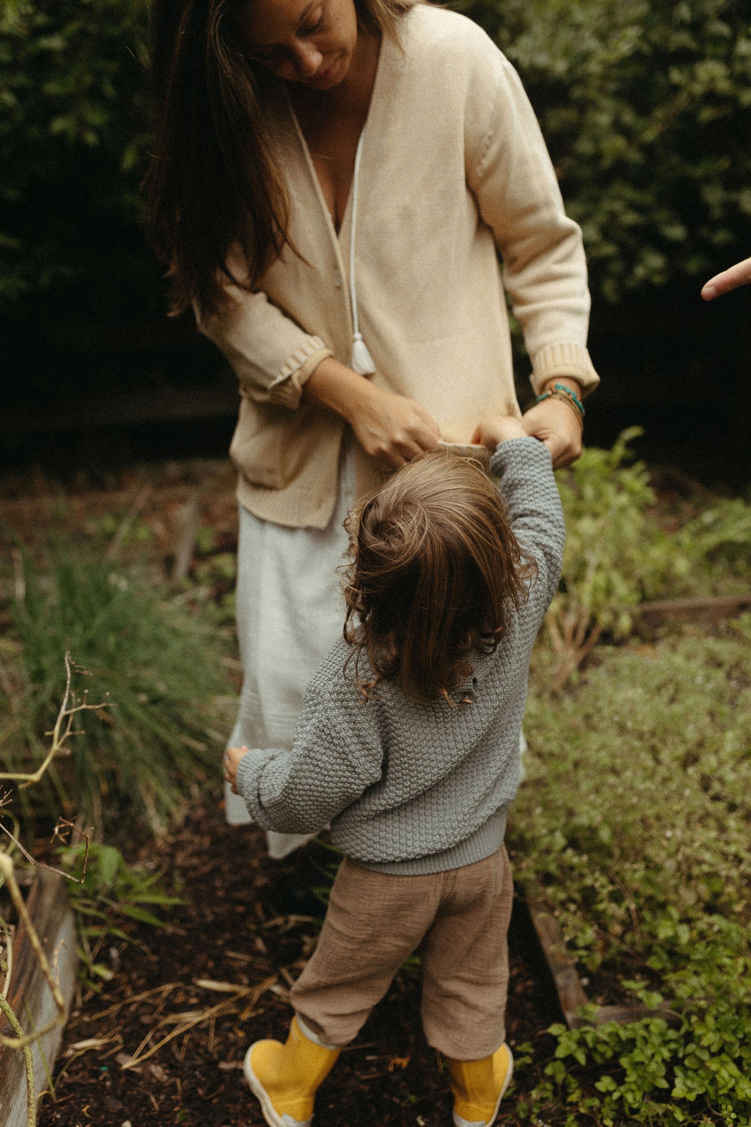 Person in cream sweater and yellow boots playing in garden setting.