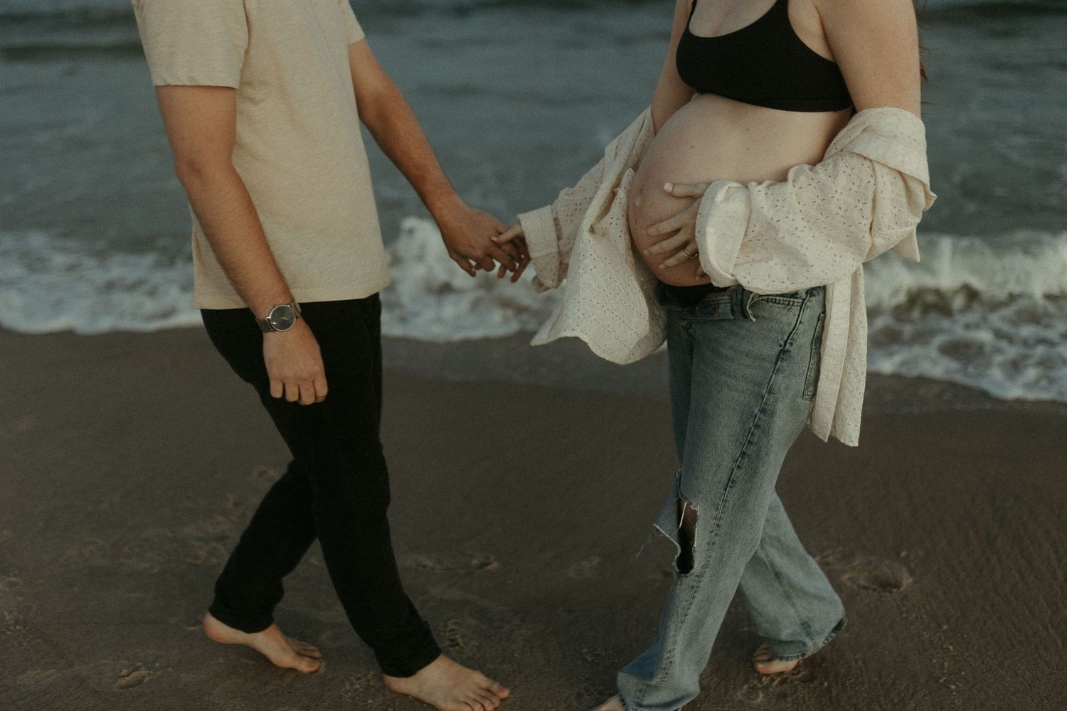 Bare feet and legs of people dancing on wet sand at the beach.