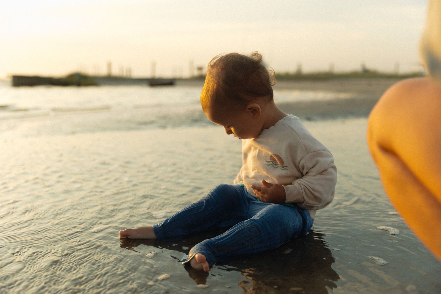 Child sitting at the edge of ocean water during golden sunset.