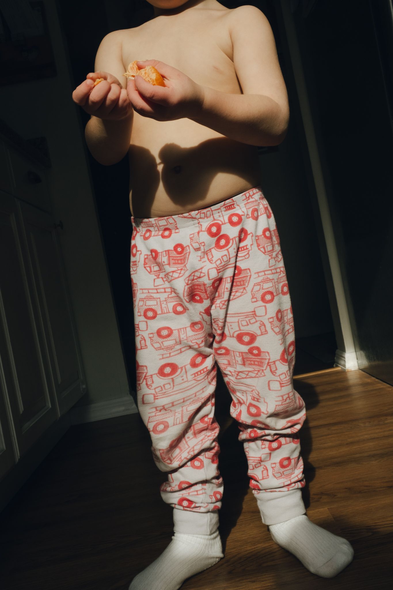 Small child wearing white and red patterned pajama pants and white socks holds something tiny in their hands.