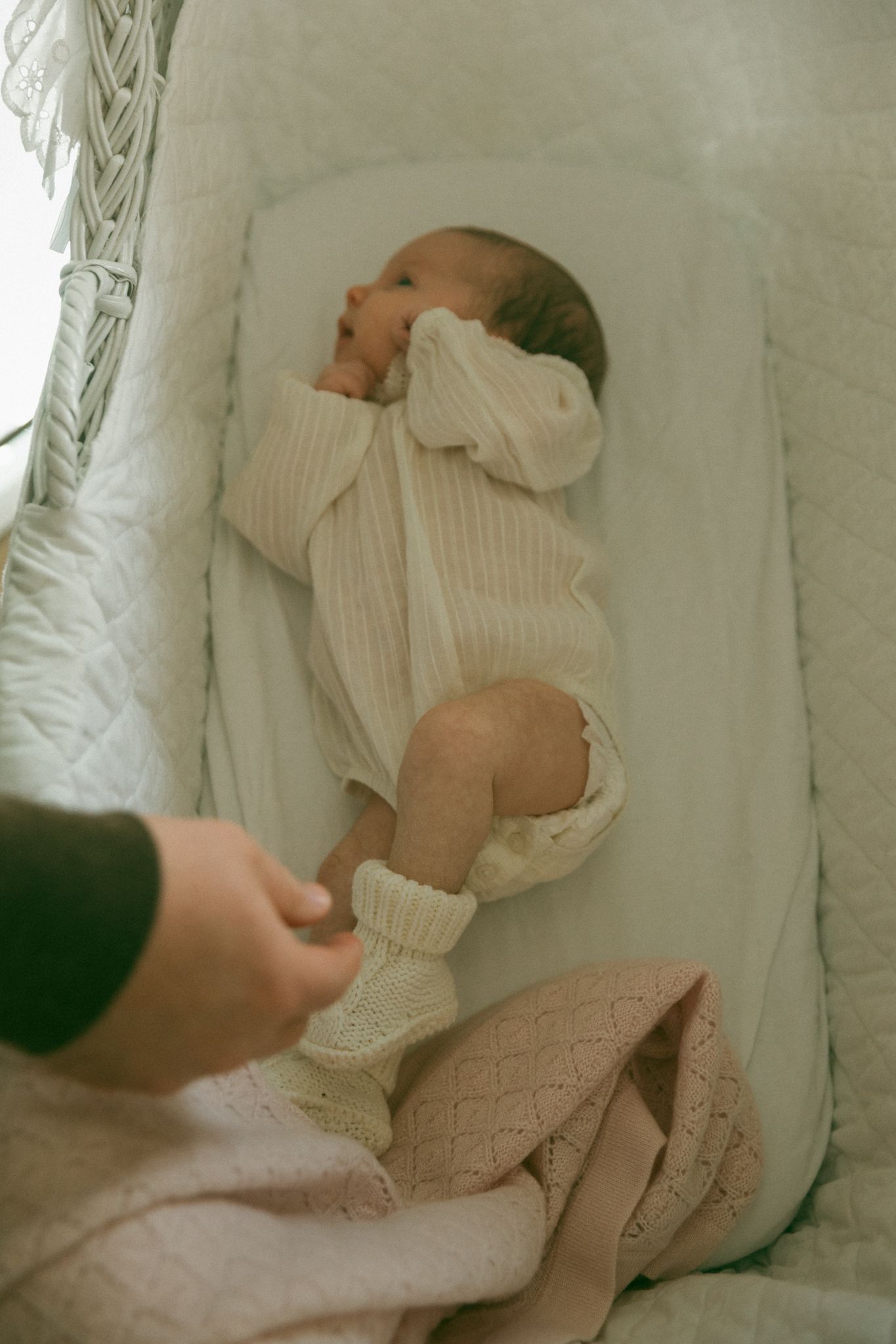 Soft knit baby clothing and blankets arranged in white bassinet.