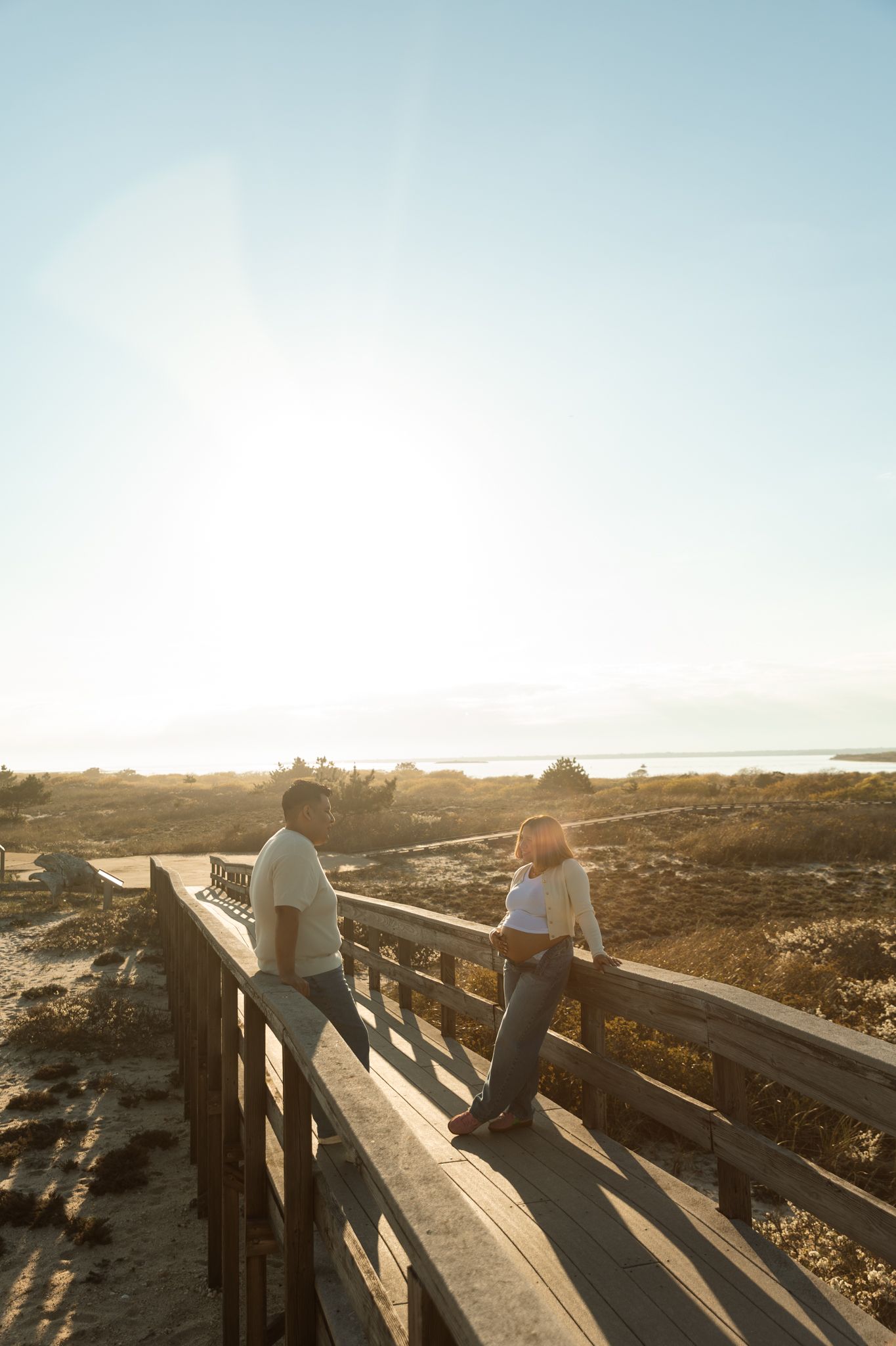 Couple standing on wooden boardwalk at sunset overlooking scenic coastal beach landscape.