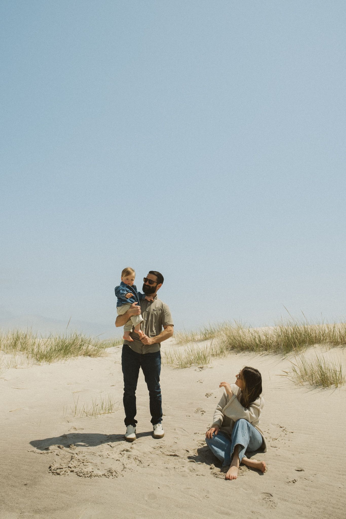 Family playing together on sandy dunes against a clear blue sky.