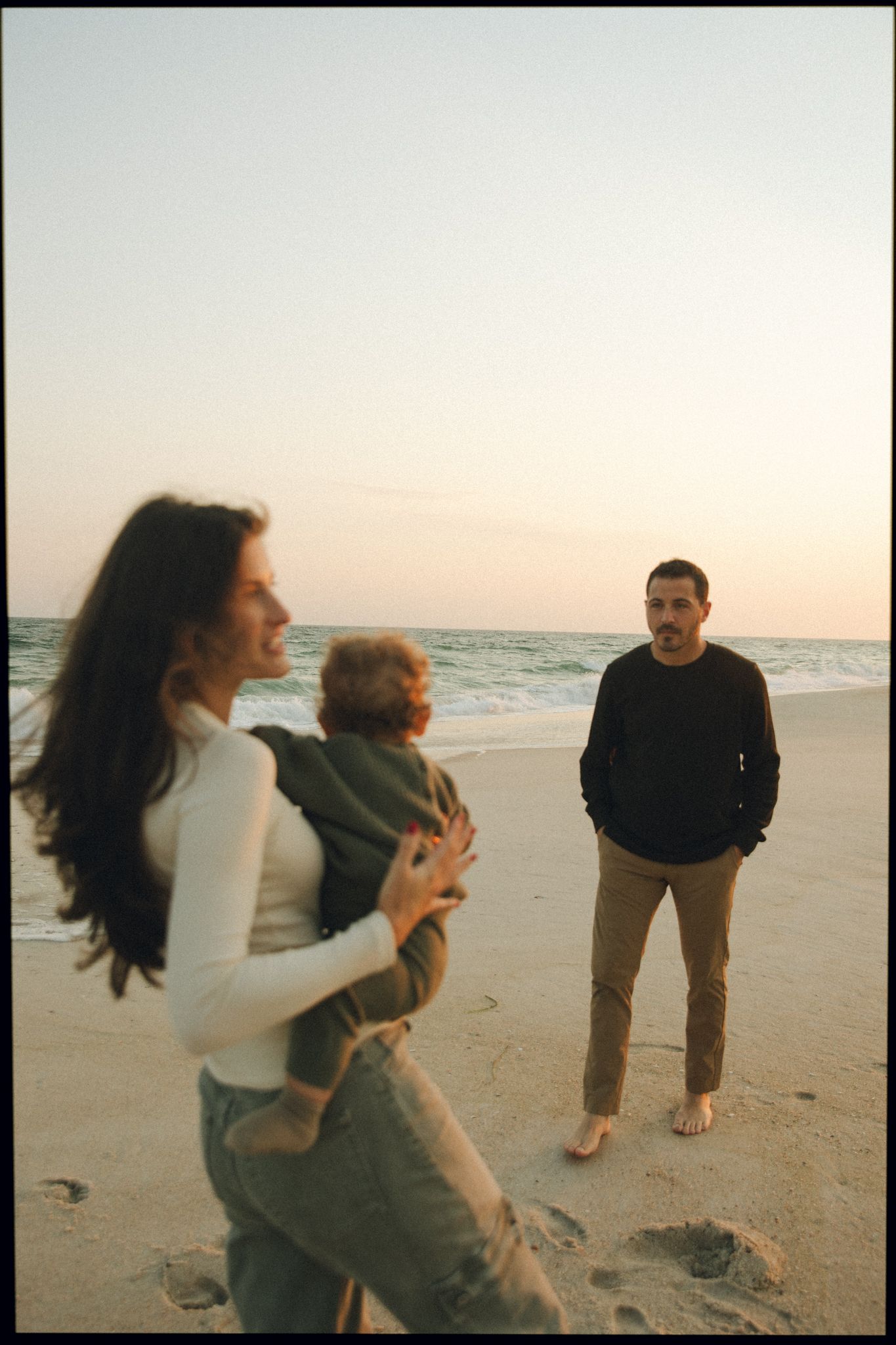 Family playing and running together on a beach at sunset.