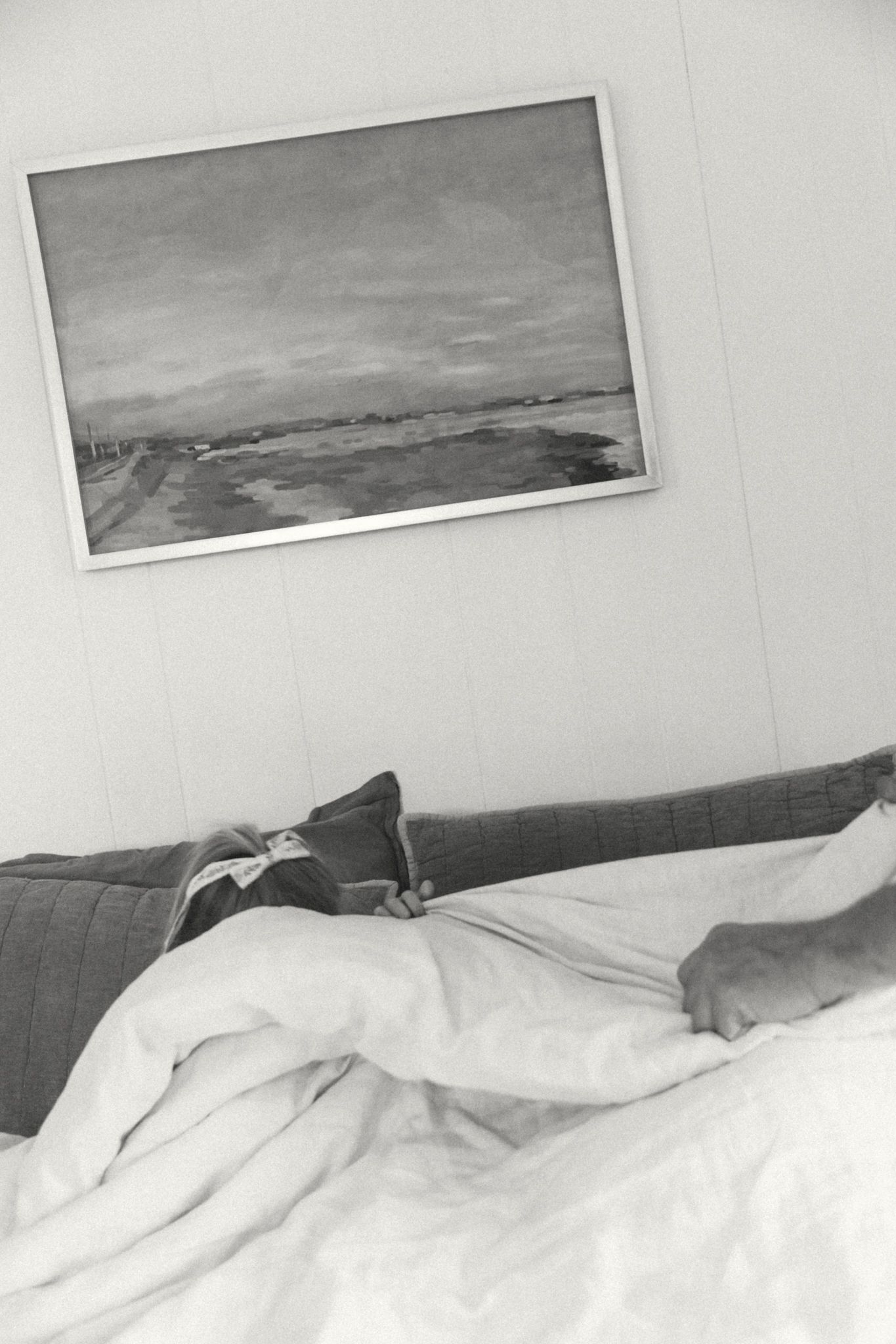 Minimalist bedroom with landscape artwork above a bed with white linens.