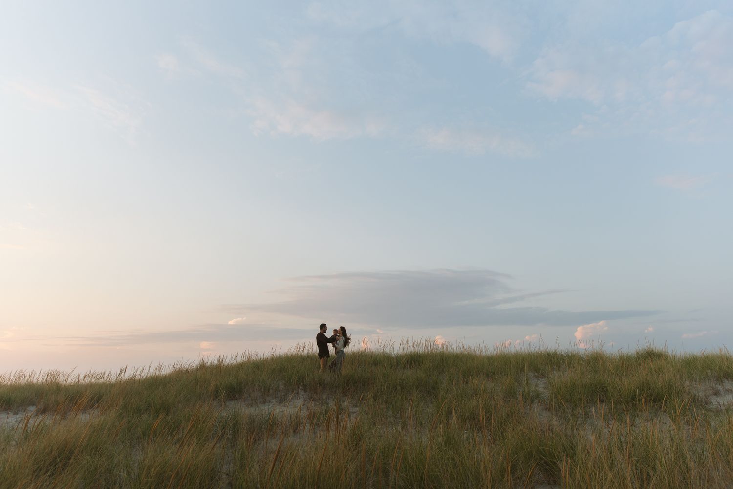 Scenic coastal landscape with grassy dunes and ocean views at sunset.