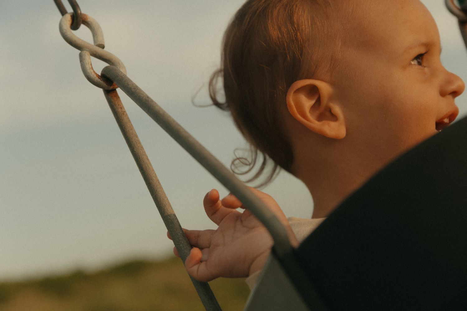 Child enjoys a swing ride against a warm sunset sky background.
