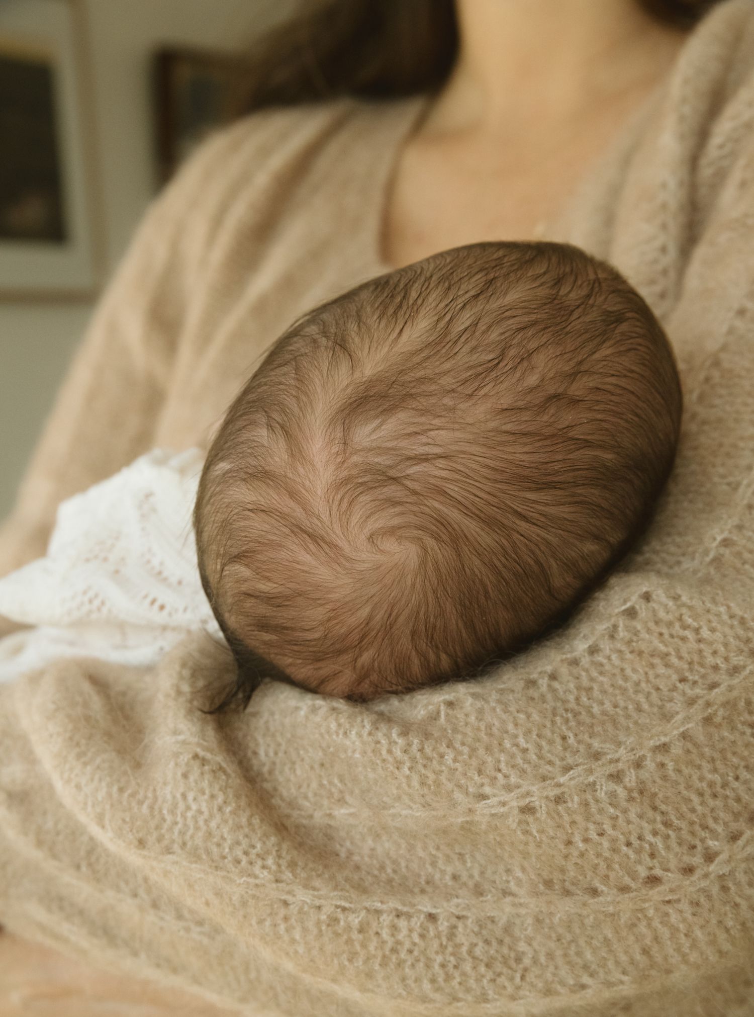 Sleeping newborn photographed against soft beige knit blanket.